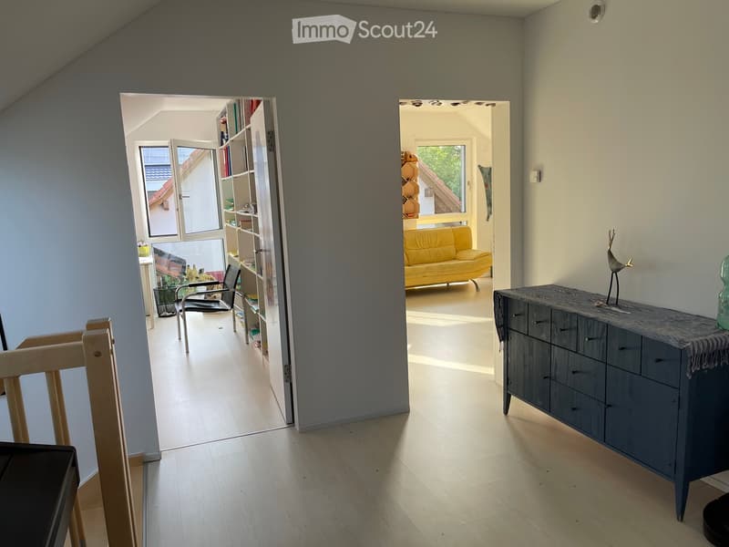 Bright hallway with wooden flooring, leading to a living room and a study area. Features a grey sideboard with decorative items, a yellow sofa, and a black chair.