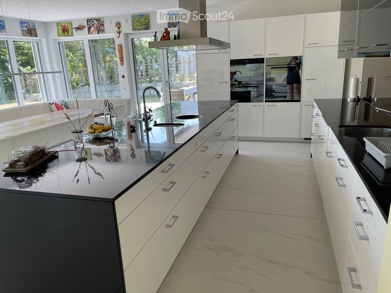 Modern kitchen with white cabinets, black countertops, and a central island. Features a built-in sofa, a sink with a modern faucet, and a large window overlooking the outdoor area.