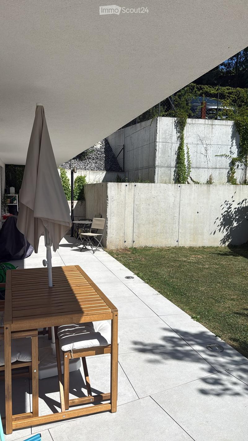 Modern outdoor patio with wooden table, chairs, umbrella, and a small grassy area.