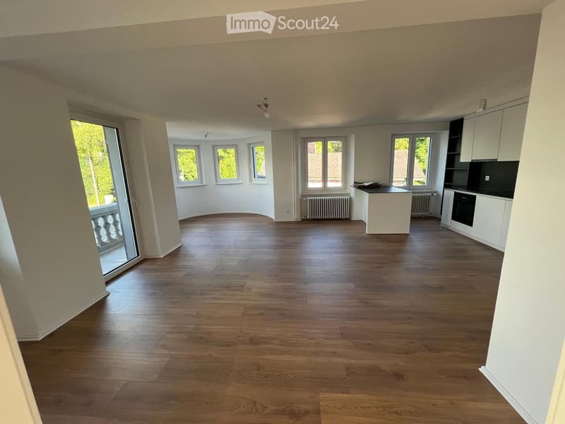 Empty room with wooden flooring, white walls, large windows, and a sliding glass door leading to a balcony.