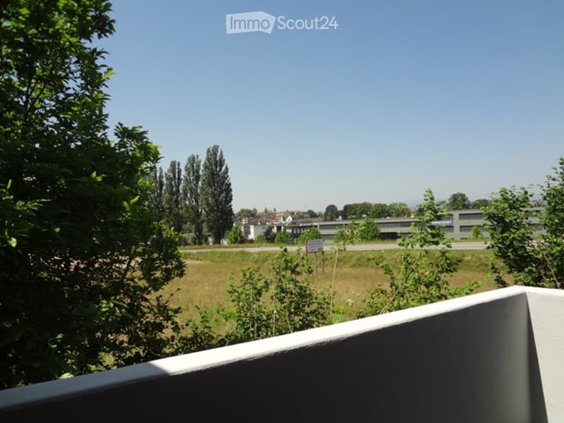 Balcony overlooking a grassy area with trees and distant buildings visible in the background.