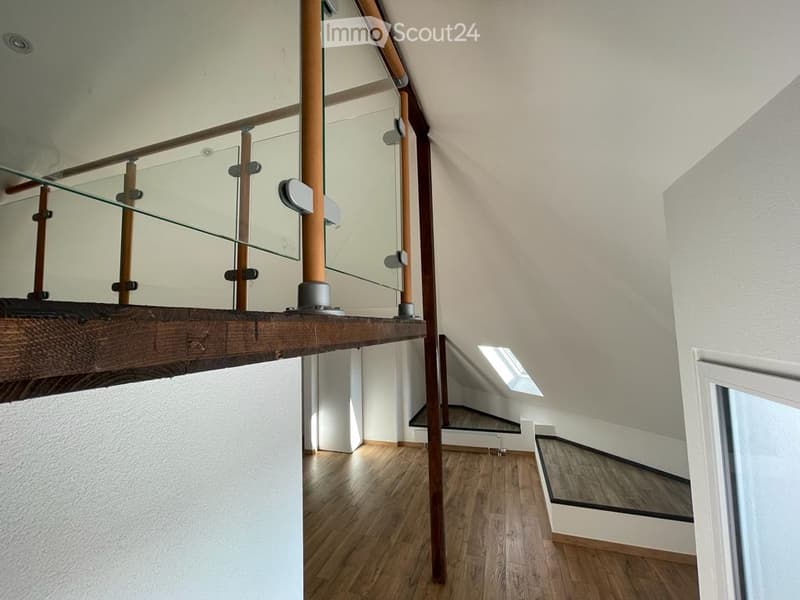 Modern hallway with wooden flooring, glass railing, and exposed wooden beams. Features a skylight and a staircase leading to an upper level.