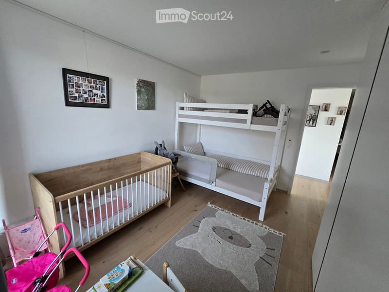 A well-lit children's bedroom with a wooden crib, a white bunk bed, a pink stroller, a soft rug, and decorative picture frames on the walls.