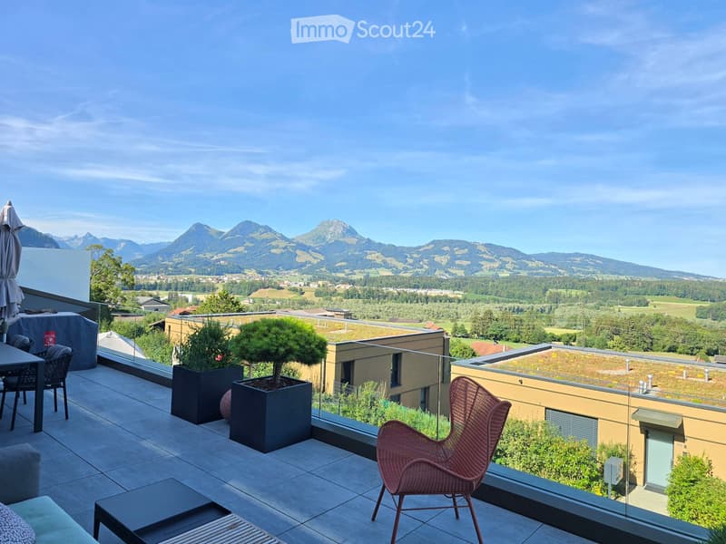 Balcony with a scenic mountain view, featuring a table, chairs, an umbrella, and potted plants.