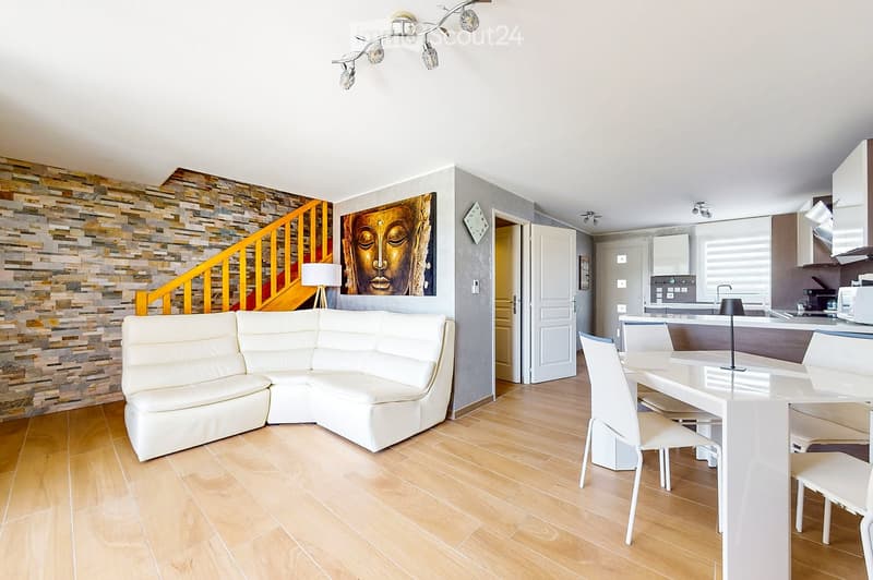Modern living and dining area with a white sectional sofa, a white dining table with chairs, a kitchen area with cabinets and appliances, and a decorative stone wall.