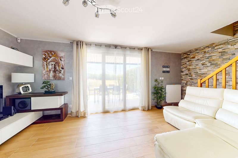 Modern living room with wooden flooring, white leather sofa, TV stand, side table with lamp, painting, and large windows with curtains.
