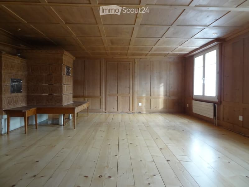 Empty room with wooden floors, wooden walls, and a large window. There are two wooden tables and built-in wooden cabinets.