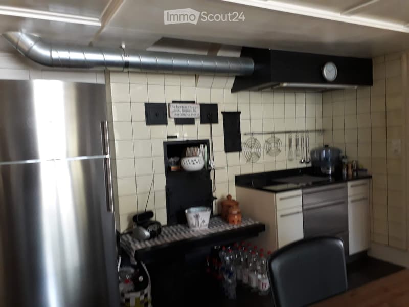Modern kitchen with white tiled walls, stainless steel appliances, and a black countertop. Features include a refrigerator, stove, oven, and various kitchen utensils and items on the counter and shelves.