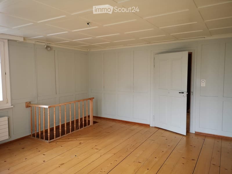 Empty room with wooden flooring, white walls, and a staircase railing. No furniture or equipment present.