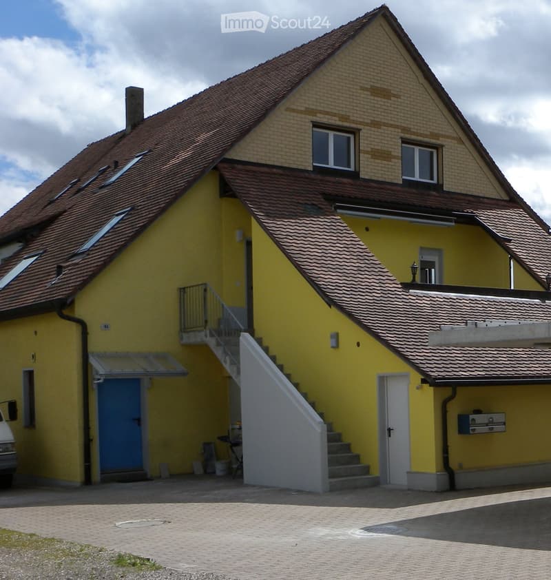 Two-story yellow house with red-tiled roof, multiple windows, and a staircase leading to an upper level.