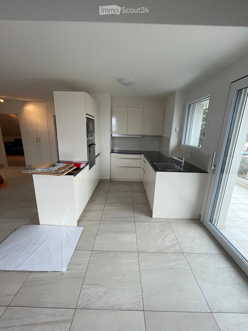 Modern kitchen with white cabinets, a central island, and a black countertop. Features include a sink with a modern faucet, an oven, and a large window providing natural light.