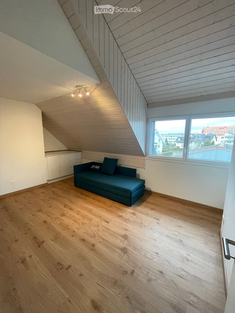 Attic room with wooden flooring, slanted wooden ceiling, large window offering a view, and a blue sofa.