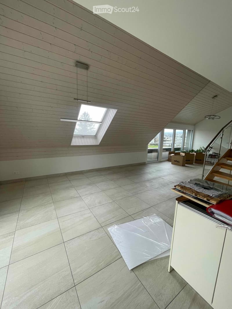 Empty room with tiled floor, wooden ceiling, skylight window, and a staircase leading upwards. Some boxes and a plastic sheet are present.