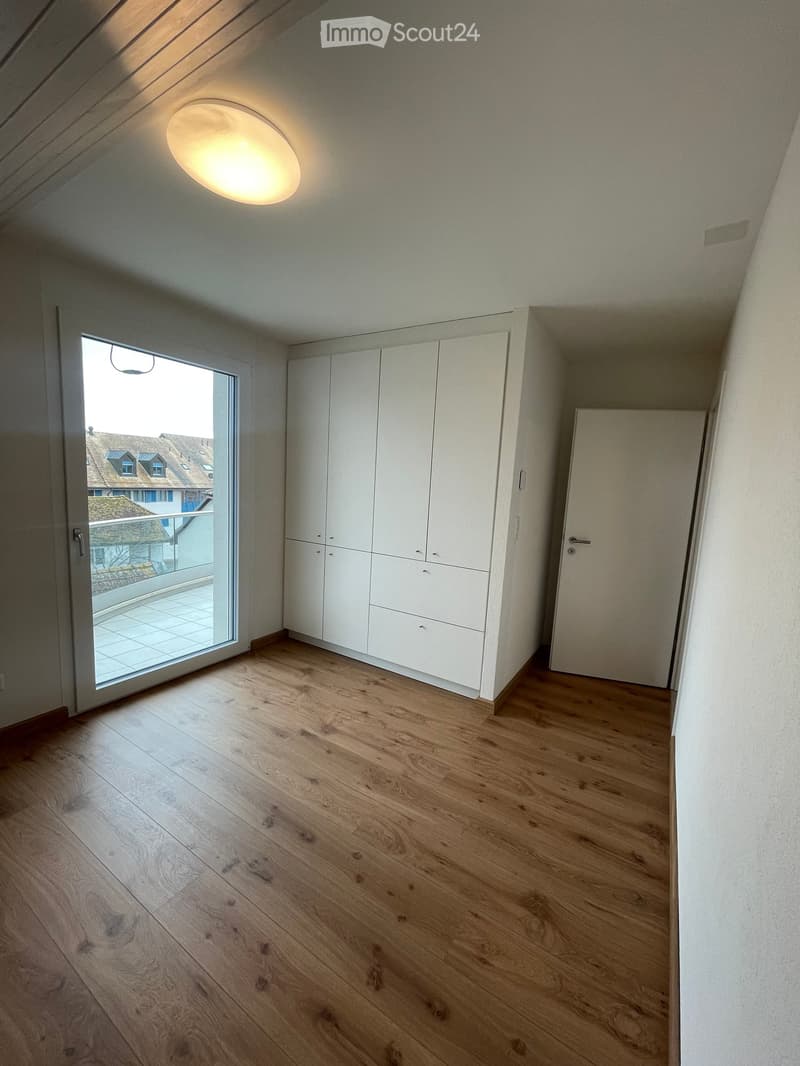 Empty room with wooden flooring, white walls, built-in white cabinetry, and a large window leading to a balcony.