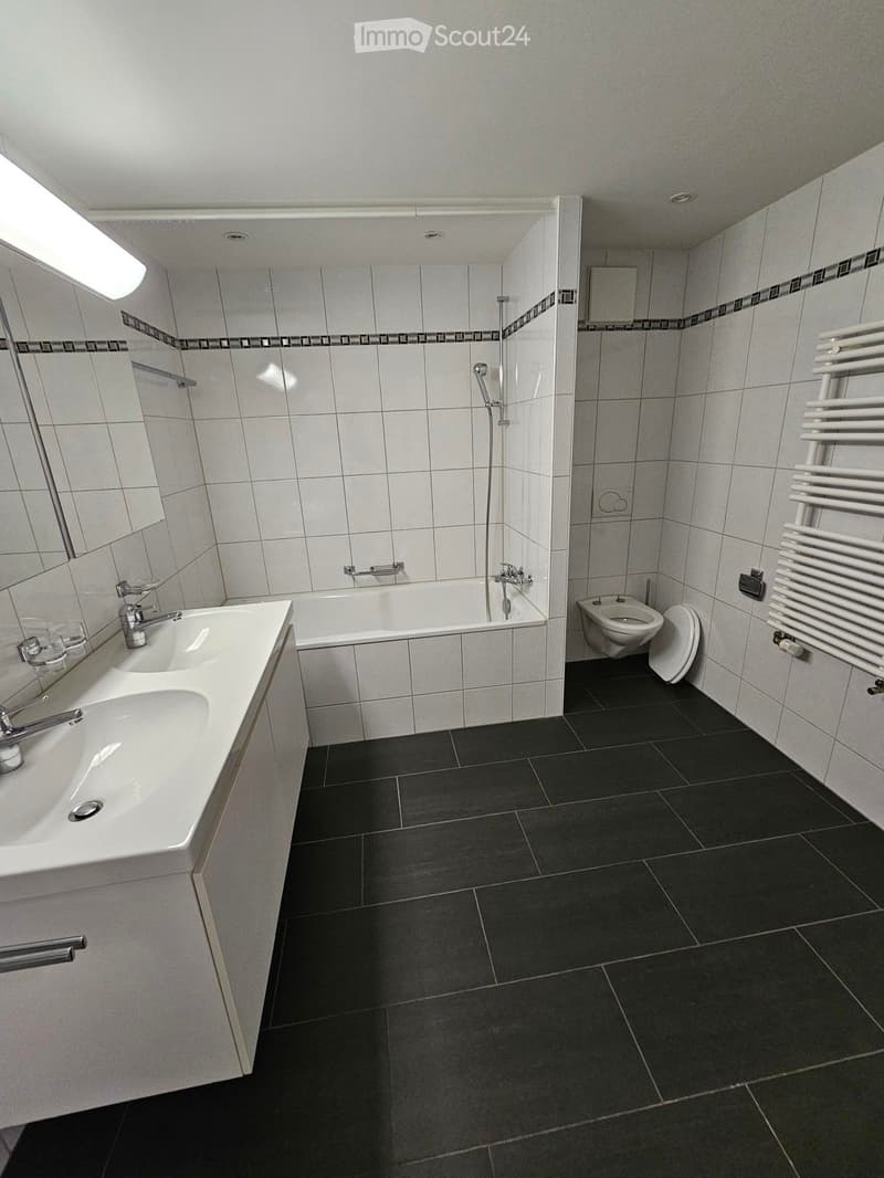 Modern bathroom with white tiles, black floor tiles, a sink, bathtub, toilet, and a radiator.