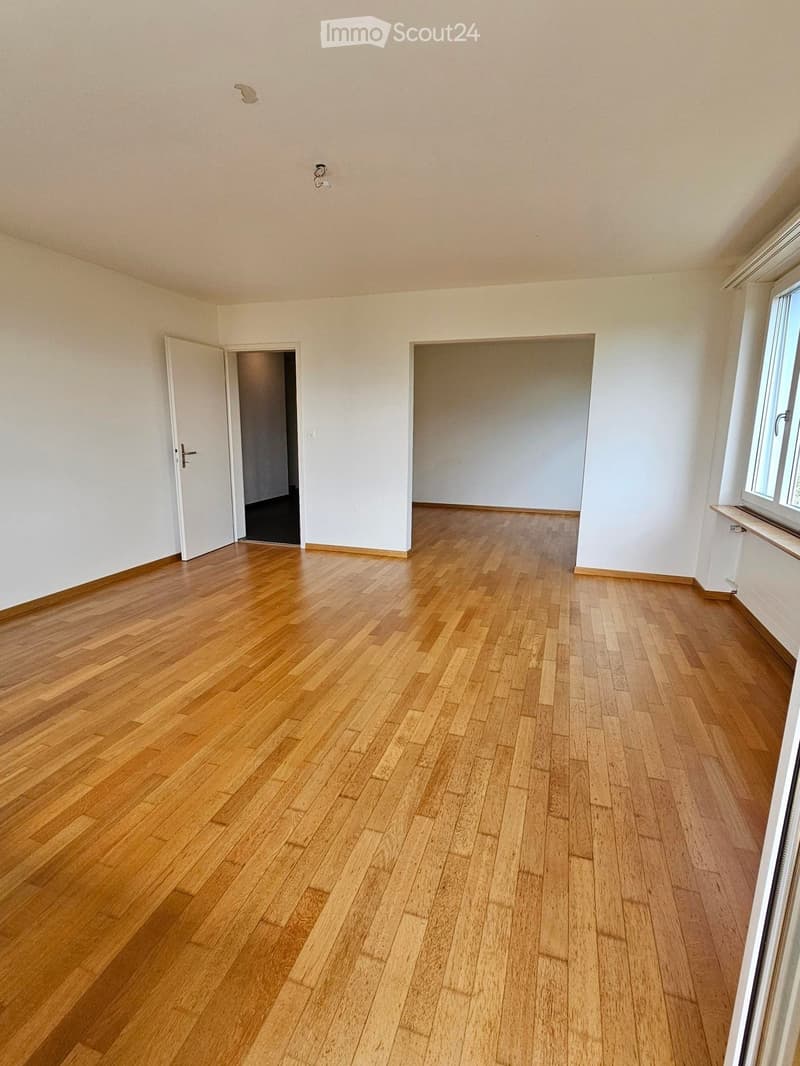Empty room with wooden flooring, white walls, and two open doors leading to other spaces.