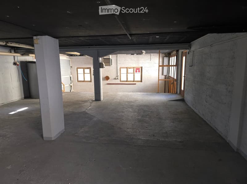 Empty room with concrete floor, white walls, and visible structural columns. Windows on one wall allow natural light to enter.