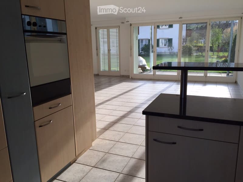 Modern kitchen with light wood cabinets, tiled floor, and large sliding glass doors leading to a garden.