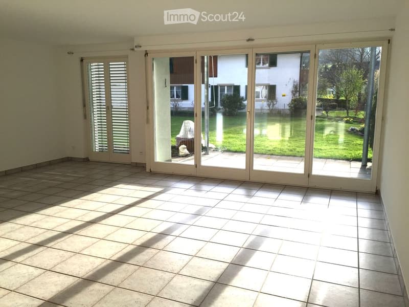 Empty room with tiled floor and large sliding glass doors leading to a garden area.