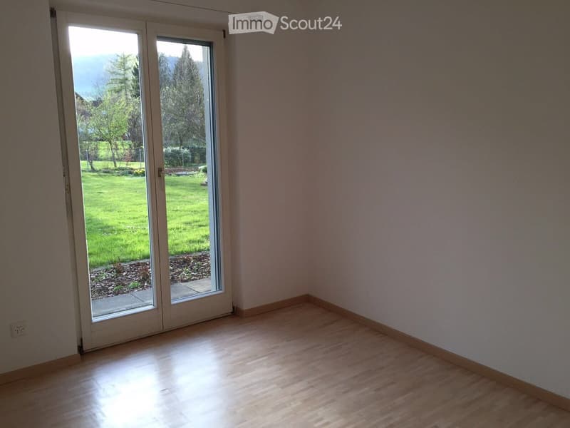 Empty room with wooden flooring, large sliding glass doors leading to a green outdoor area.