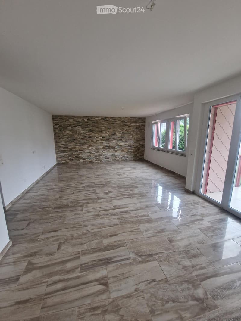 Empty room with polished tile flooring, white walls, and large windows with blinds. A stone accent wall is visible on one side.