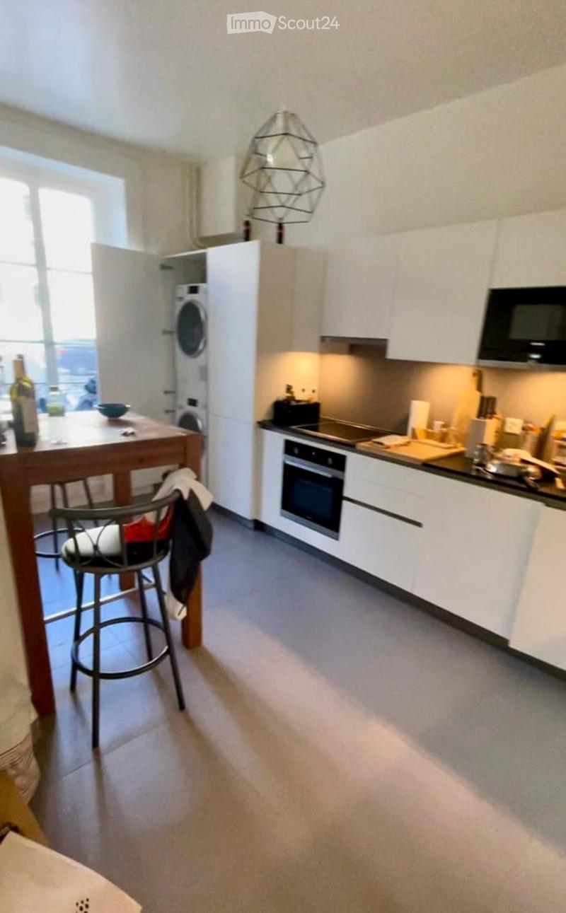 Modern kitchen with white cabinets, stainless steel appliances, a bar stool, and a small dining area with a table and chairs.