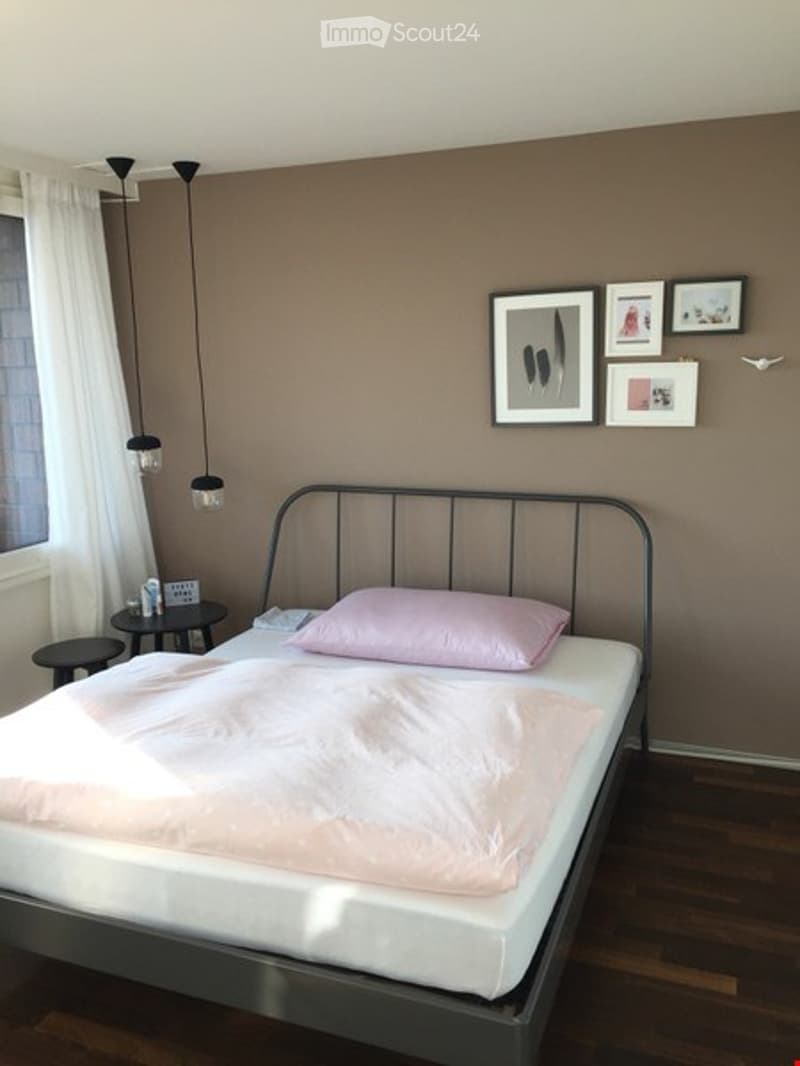 Bedroom with a metal-framed bed, pink bedding, nightstand, stool, and wall-mounted picture frames.