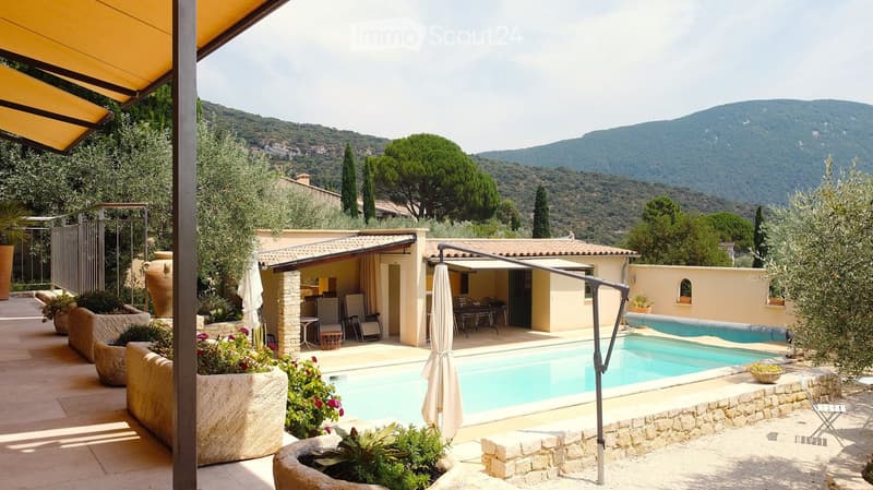 Outdoor garden area with a swimming pool, lounge chairs, potted plants, and a scenic mountain view in the background.