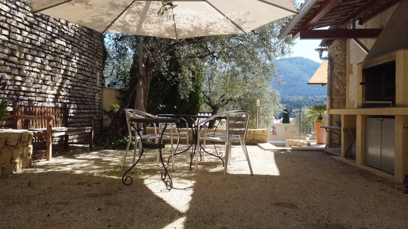 Outdoor patio with stone walls, wooden bench, metal table and chairs, umbrella, and scenic mountain view.