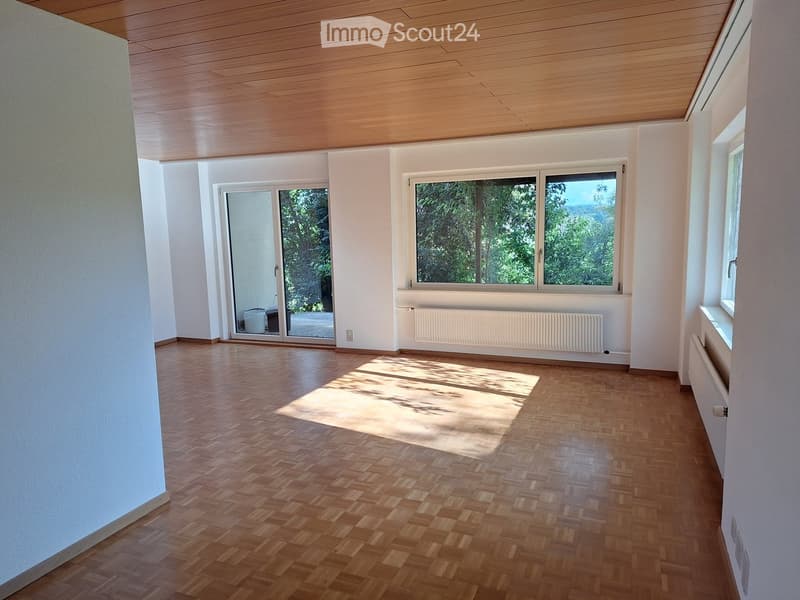 Empty room with wooden flooring, white walls, large windows, and a sliding glass door leading outside.