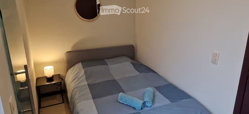 Cozy bedroom with a single bed, nightstand, lamp, and a round mirror on the wall.