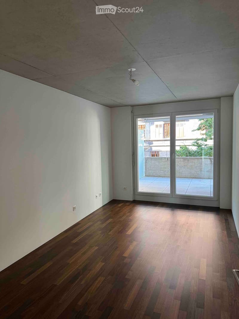 Empty room with wooden flooring, white walls, and a large sliding glass door leading to a balcony.