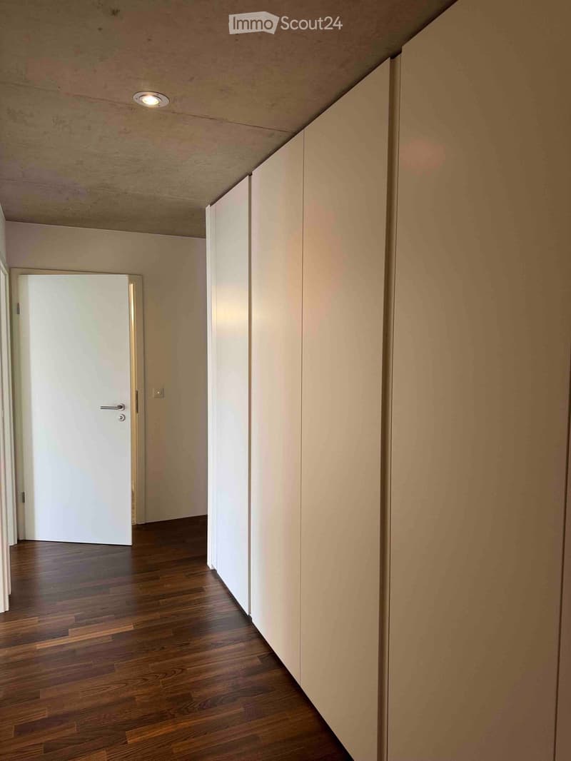 Empty hallway with wooden flooring, white walls, and a closed white door at the end.