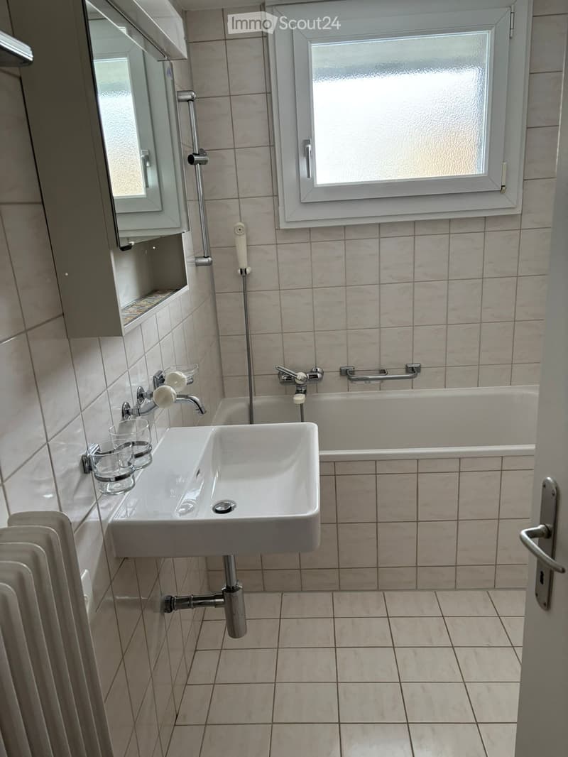 Modern bathroom with a white bathtub, sink, and tiled floor, wall-mounted mirror and towel rack.