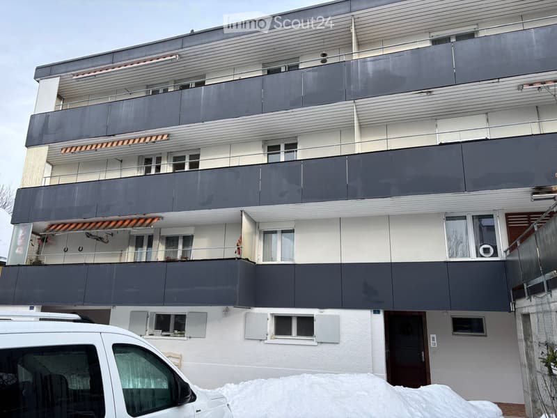 multi-storey building, 4 floors, grey and white color, several balconies, covered parking area