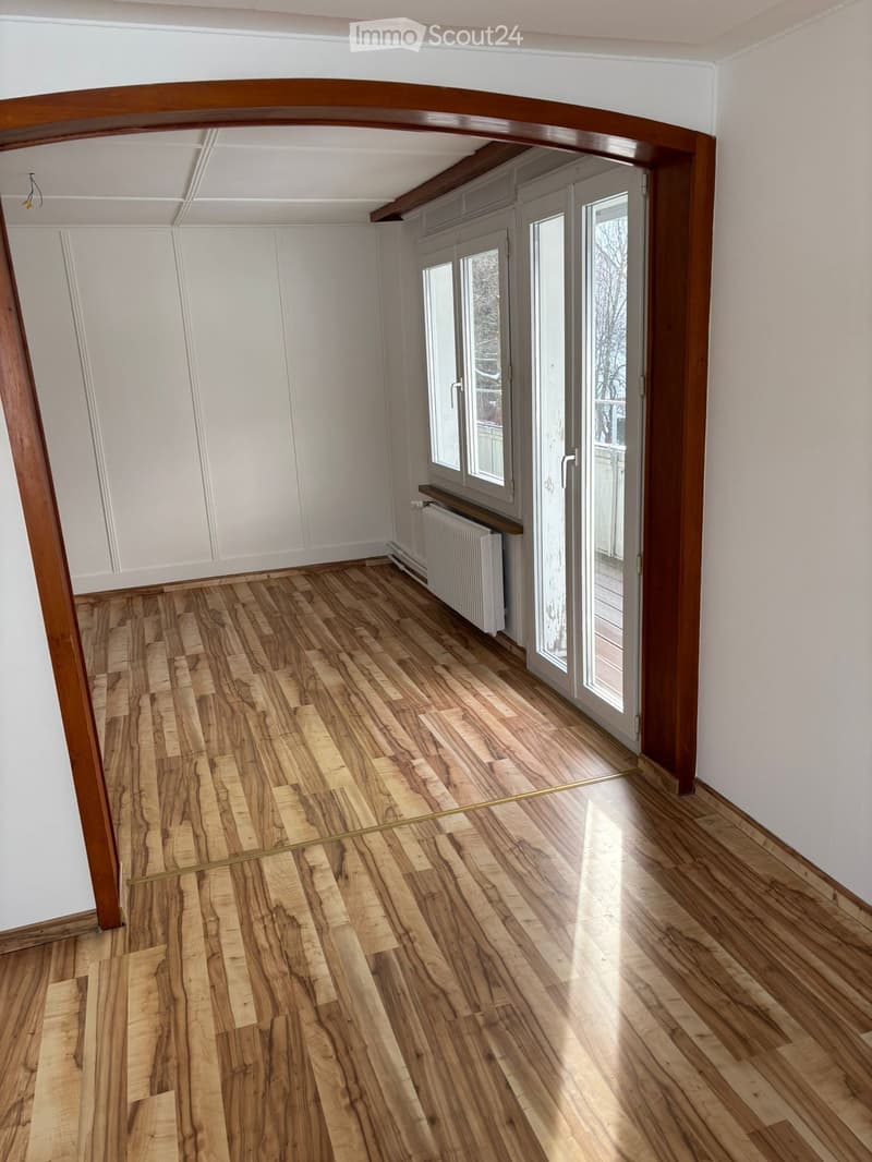 Empty room with wooden floor, sliding doors, white walls, balcony, radiator