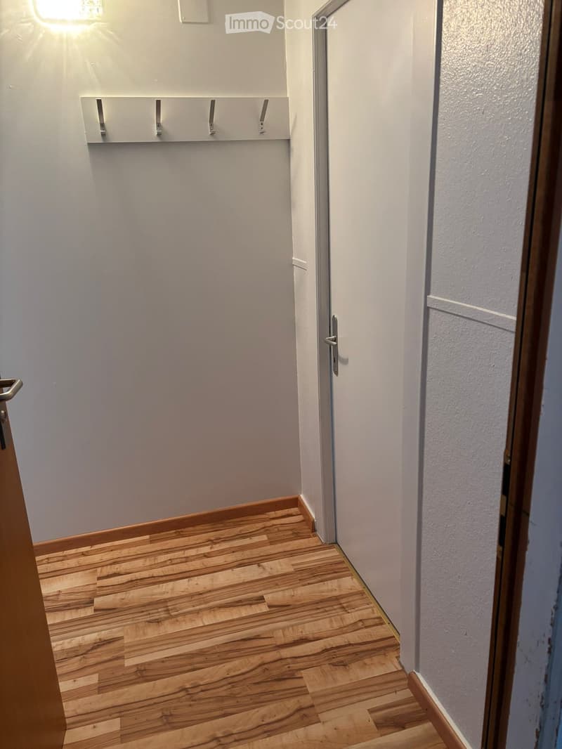 Corridor with wooden floor, white walls, metal railings, and an open door.