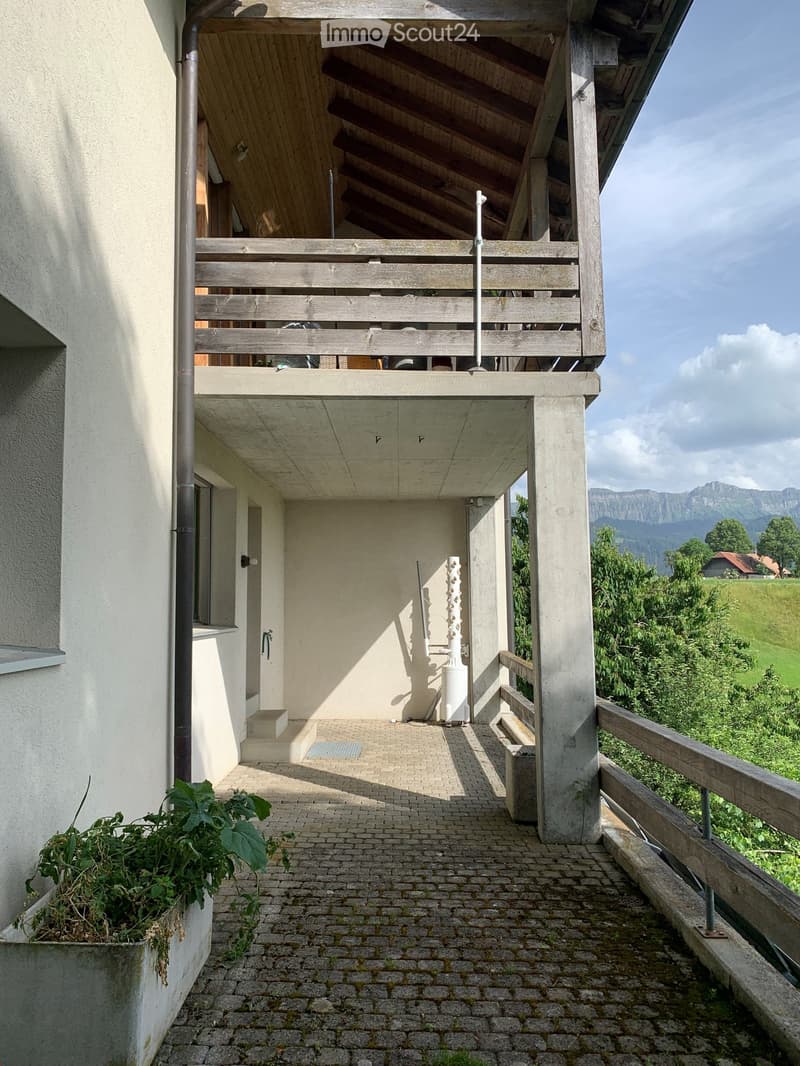 Brick-paved balcony with wooden railing, overlooking a green landscape and mountains.