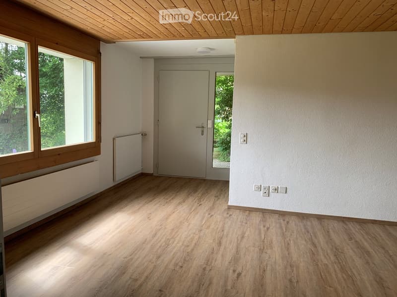 Empty room with wooden flooring, white walls, large windows, and a door leading to another space.