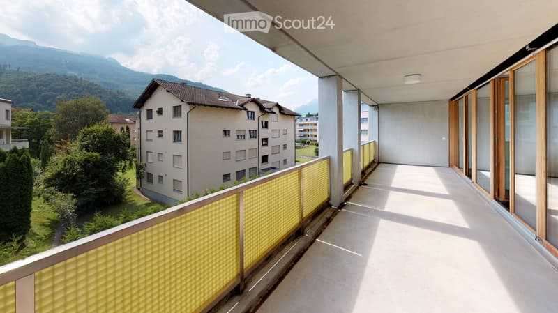 Balcony with yellow glass balustrade, overlooking a residential area with buildings and mountains in the background.