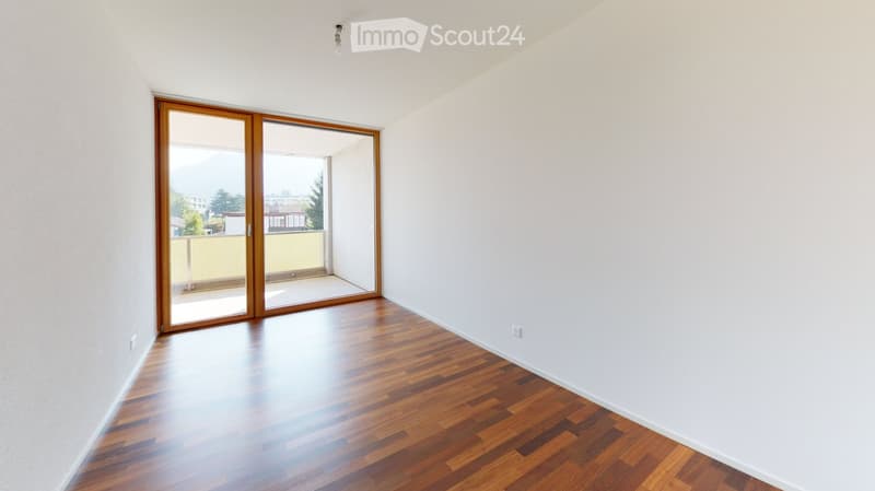 Empty room with wooden flooring, white walls, and large sliding glass doors leading to a balcony.