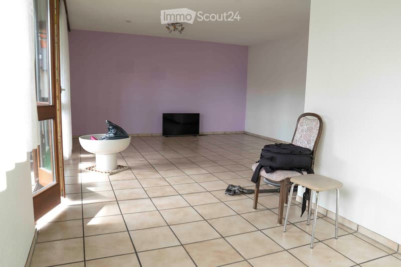 empty room, large tiled floor, light purple and white walls, television against wall, small table and chair by wall