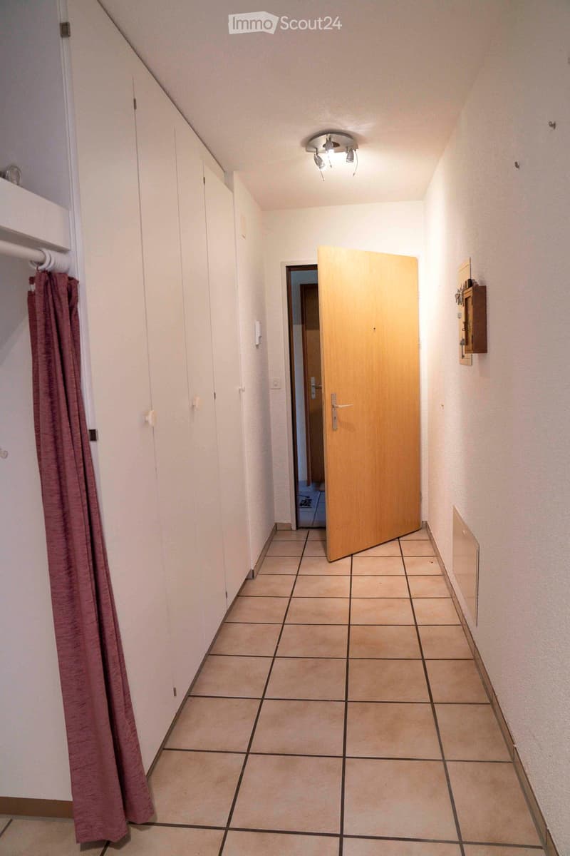 An empty hallway, with white cabinets, a hallway door leading to another room, white walls, and tiled flooring