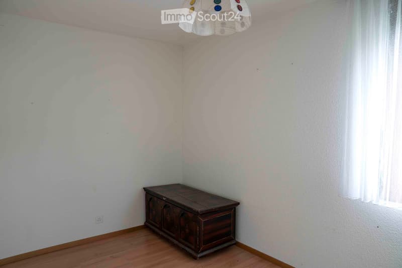Empty room with white walls, wooden floor, wooden chest, power outlet, lamp.