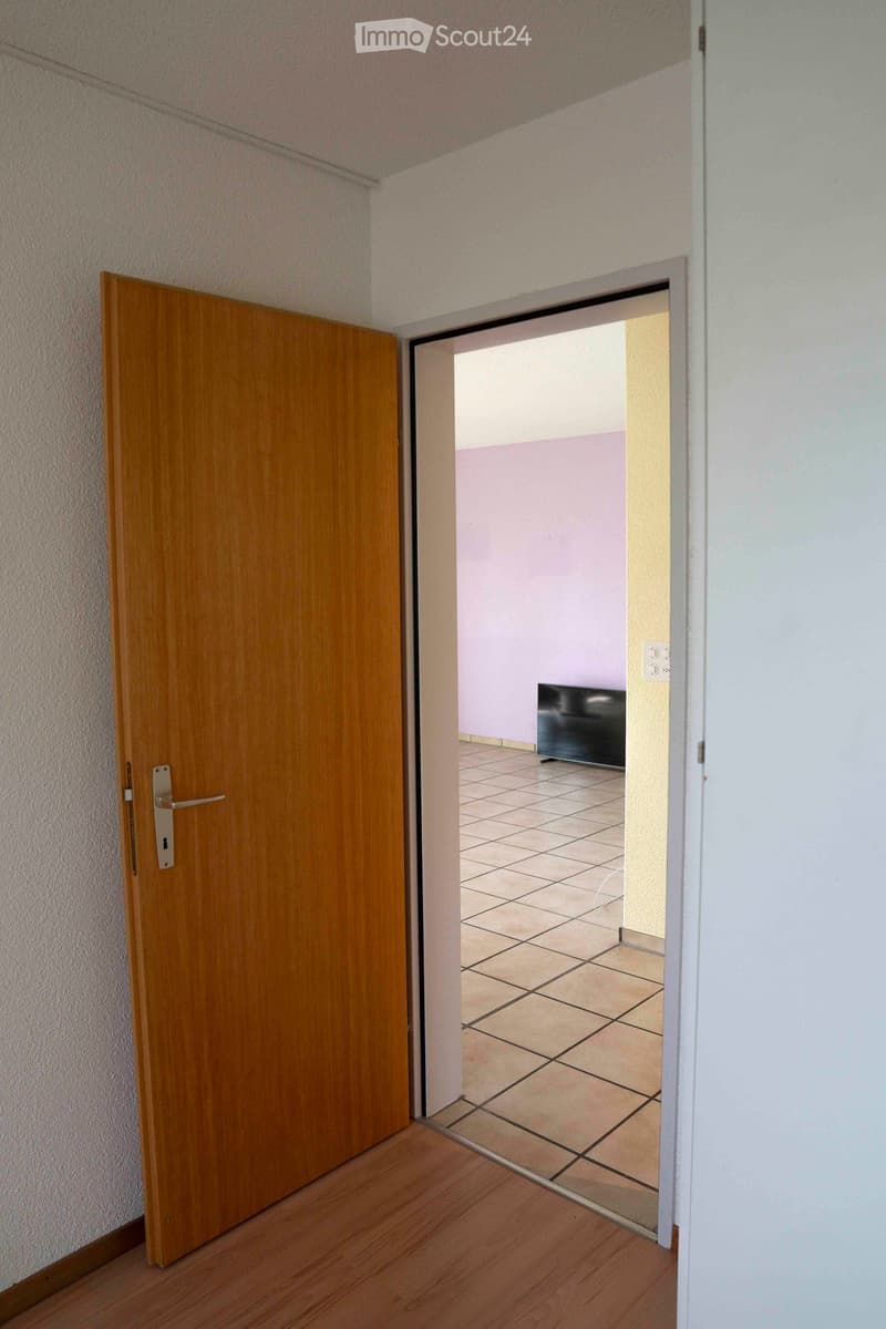 open door, adjacent room, tiled floor, beige tiles, white walls, small black TV