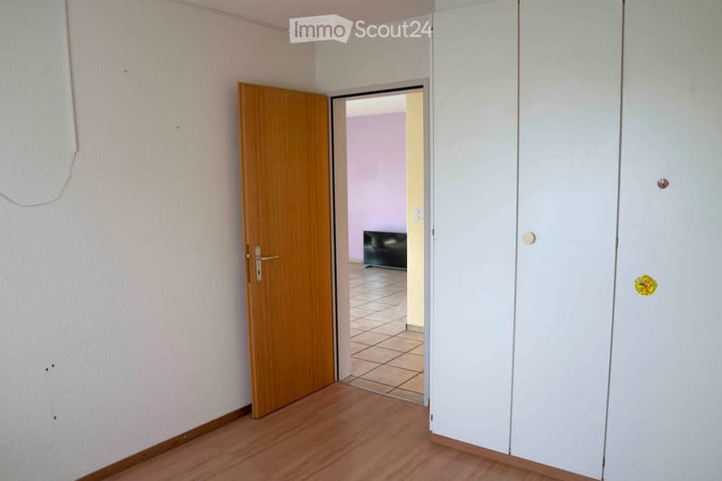 Empty room, wooden door, white wardrobe, tiled hallway, door to adjacent room with TV