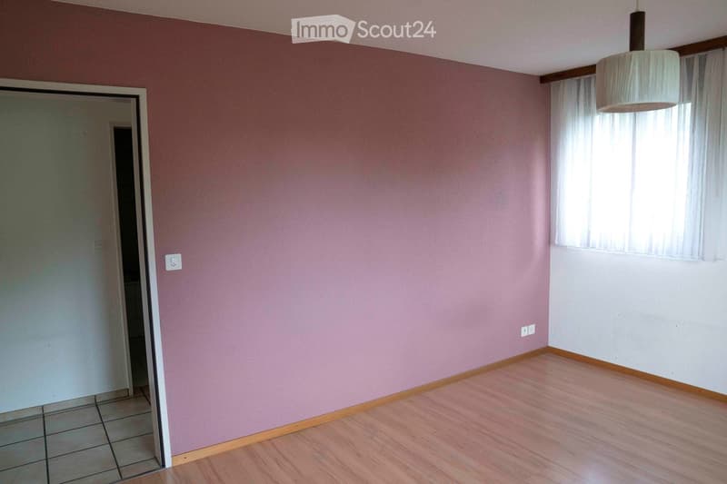 empty room with pink walls, wooden floor, open door, power outlets, and a window with curtains