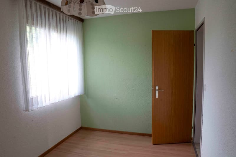 Empty room with green and white walls, wooden floor, and white curtains