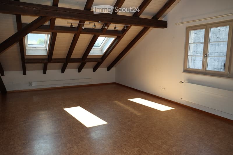 Empty attic room with wooden beams, skylights, and natural light. Bare walls and floor, no furniture or equipment.