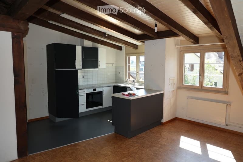 Modern kitchen with dark cabinets, stainless steel appliances, and a central island. Exposed wooden beams on the ceiling and large windows provide natural light.